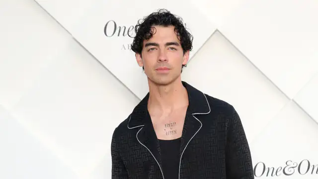 Joe jonas is wearing jeans and a jacket while performing with his brothers